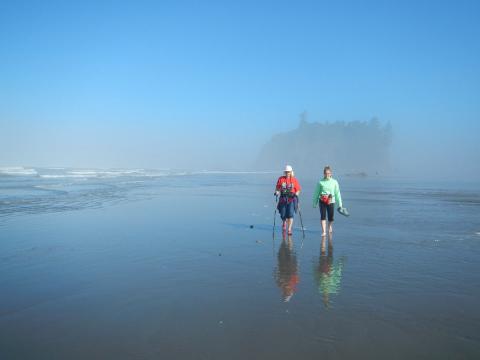 Two hikers on a foggy beach in Olympic National Park with an island in the background 