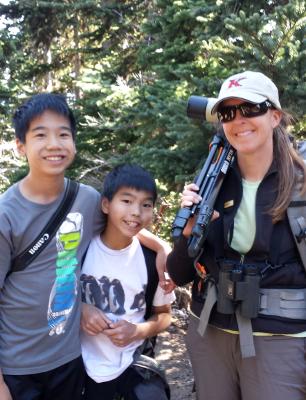 Wildlife guide Carolyn who has a spotting scope over her shoulder stands with two young participants on the Hurricane Hill trail