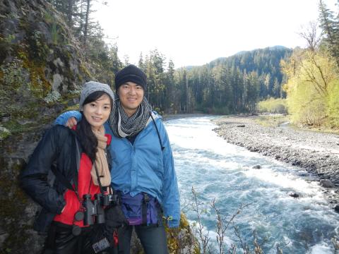 Two hikers pose next to the Elwha River riparian area that includes gravel bar and deciduous trees like Red Alder