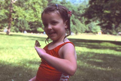 Carolyn as a child smiling in her bathing suit with a butterfly on her hand