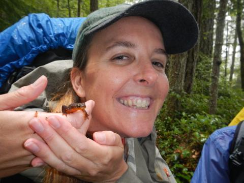 Hiking Guide Carolyn smiling and gently holding a small Rough-skinned Newt that has a bright orange belly