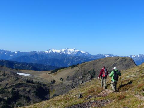 Hikers on a small narrow alpine trail with Mount Olympus in the background