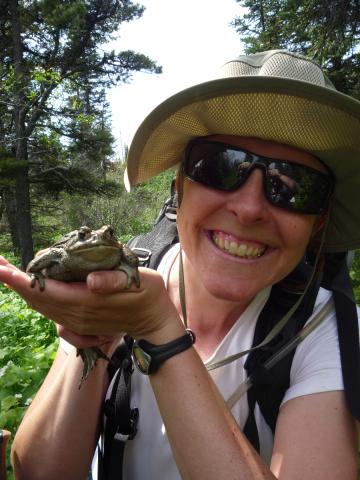 Your hiking guide Carolyn smiling and gently cradling a large Western Toad in her hands